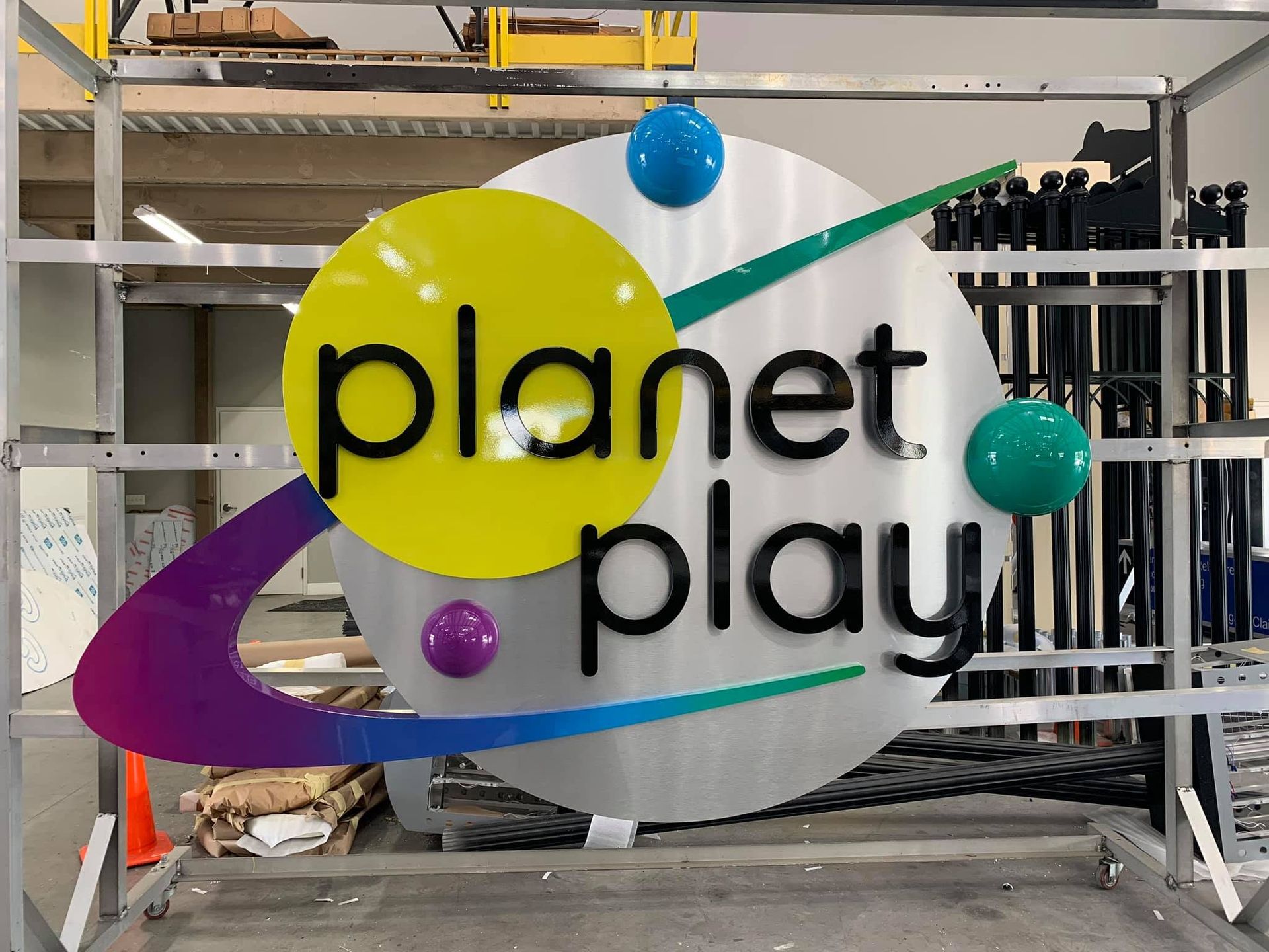 Planet Play logo sign with yellow, purple, teal, and white circular design on a metal shelf