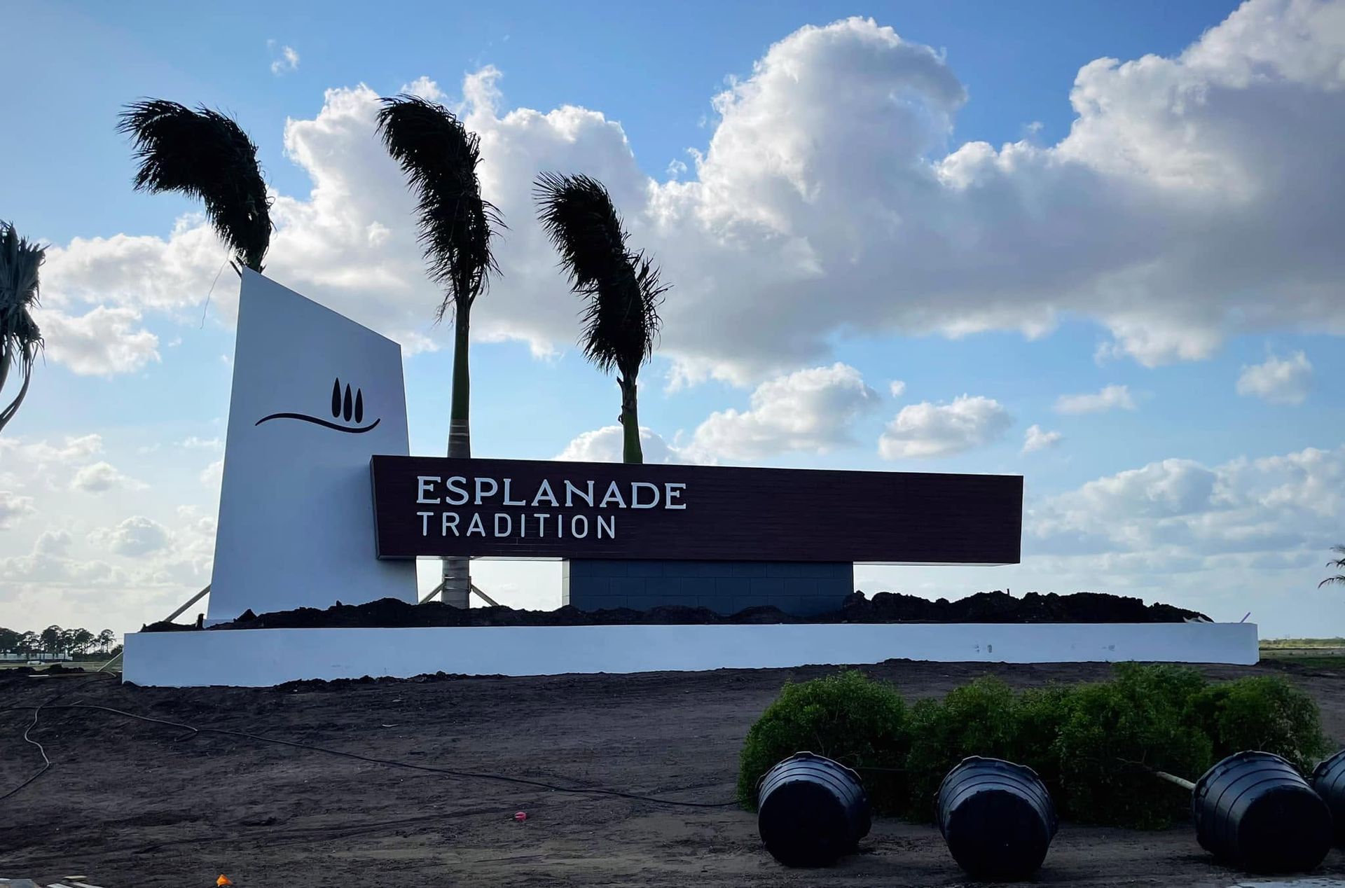 Esplanade Tradition sign on a white monument by palm trees under a partly cloudy sky.