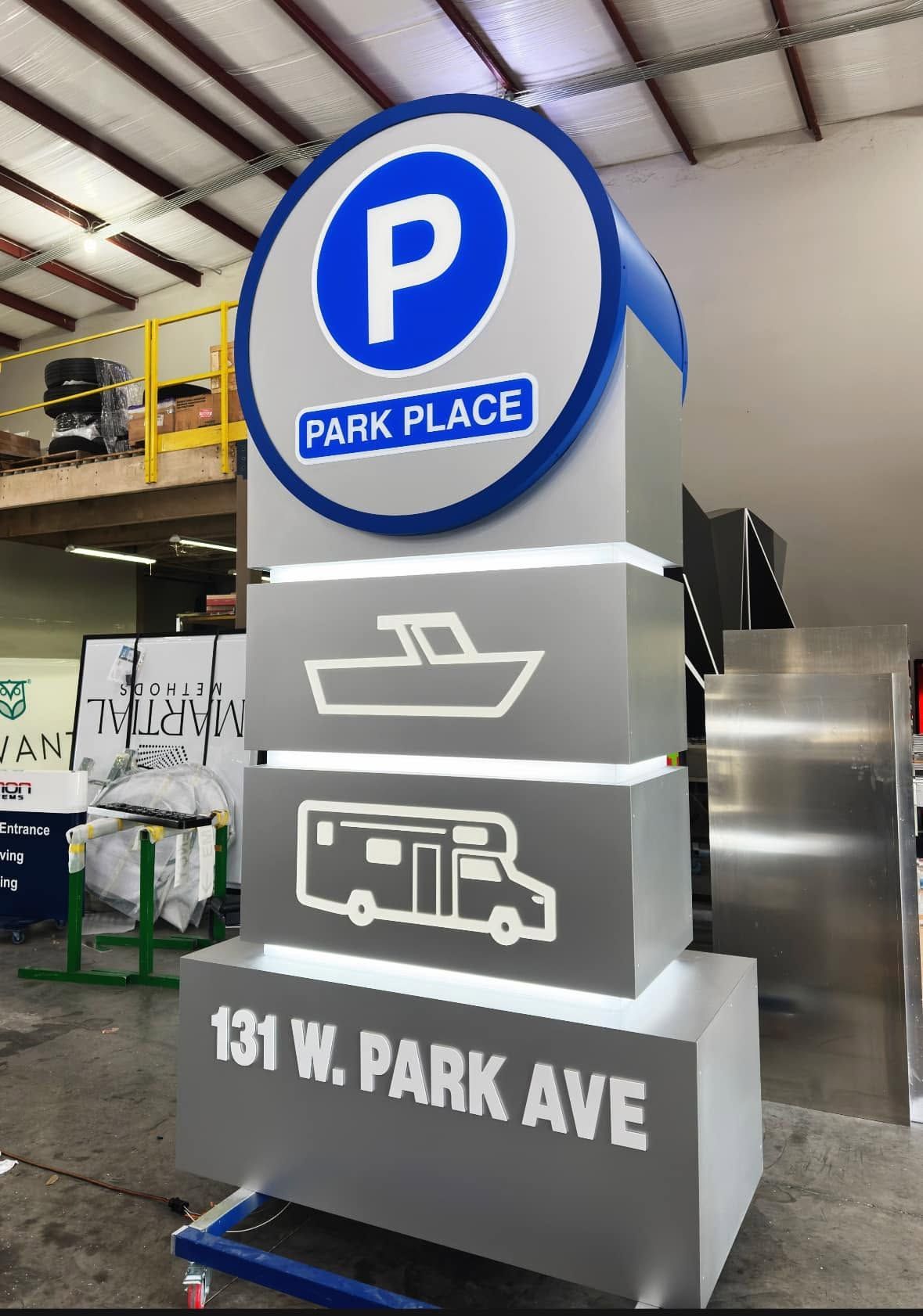 Parking sign with blue PARK PLACE logo, boat and RV icons, and address 131 W. Park Ave.