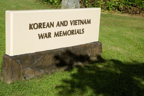 Korean and Vietnam War memorial sign on a stone base in a grassy park