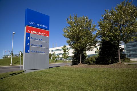 A blue corporate sign beside a grassy lawn and trees in front of an office building.