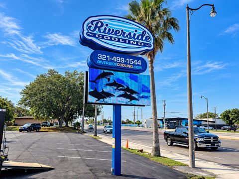 Riverside sign along a roadside under a bright blue sky, with cars and palm trees nearby