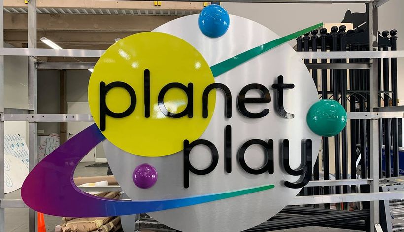 “planet play” logo on a white sign with colorful spheres and a purple swoosh in an indoor setting
