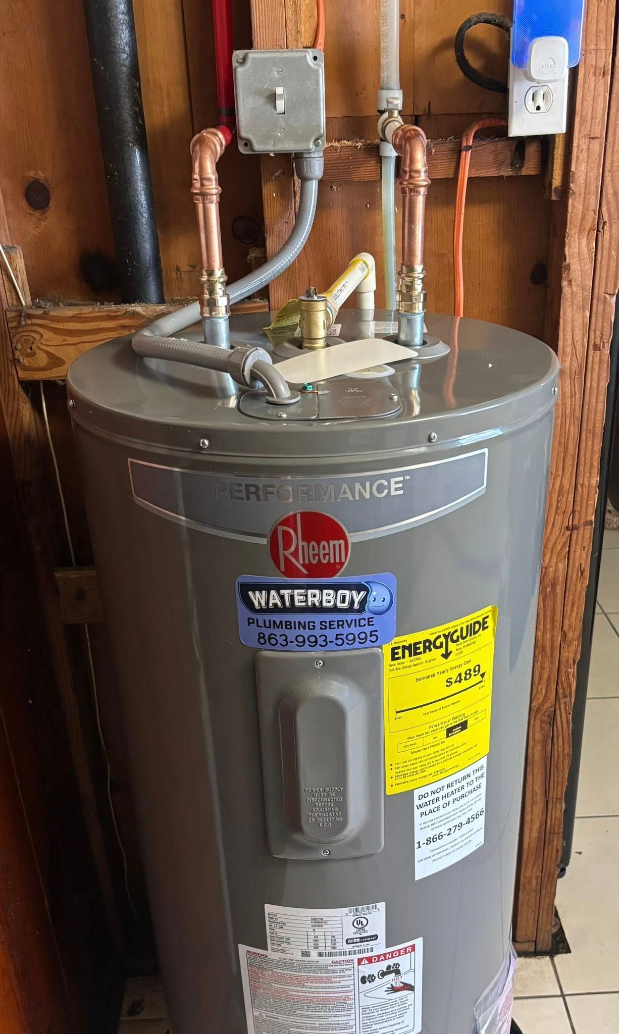 Gray Rheem water heater with copper pipes in a utility closet.