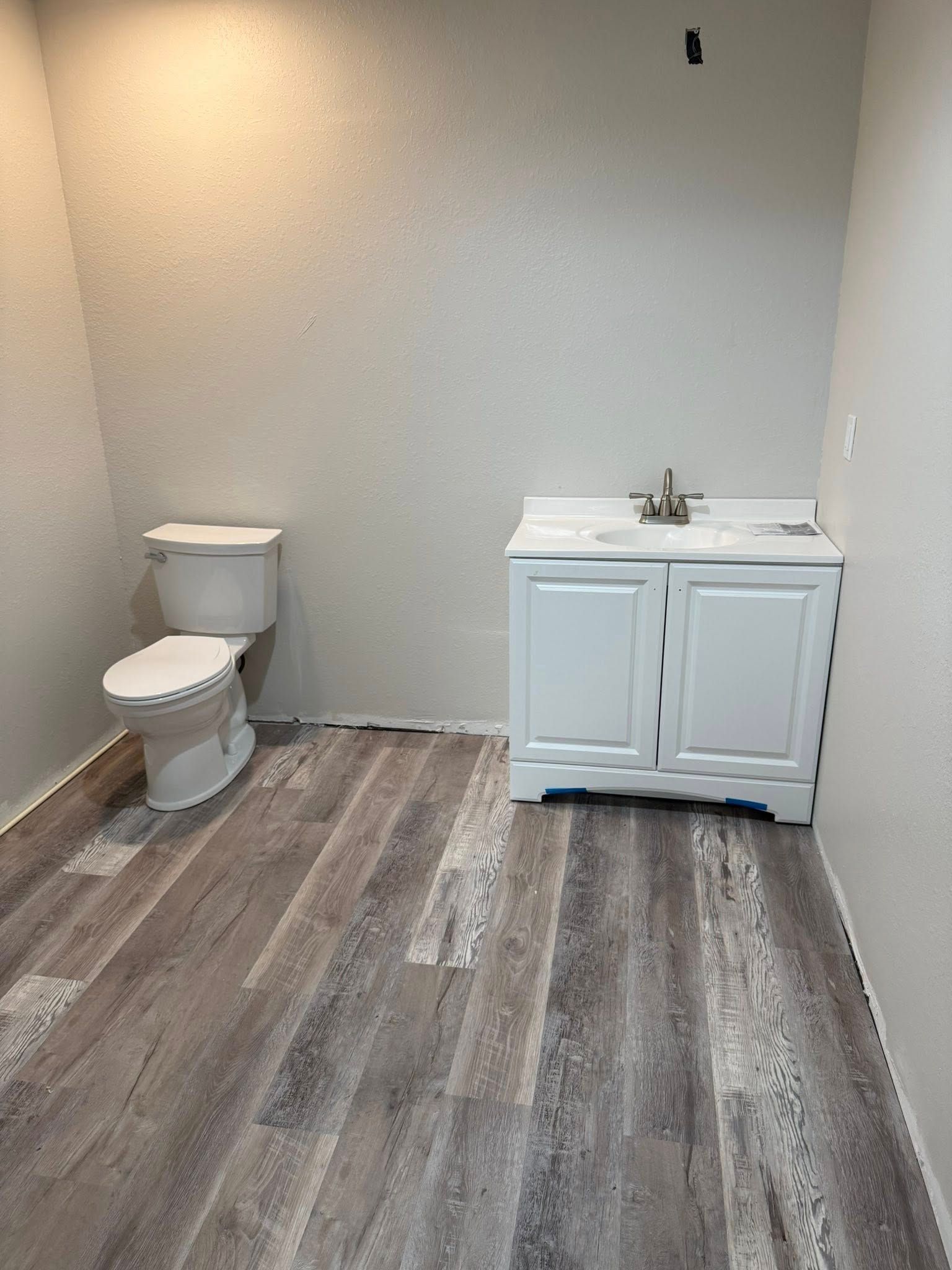 Bathroom with white toilet and vanity against light gray walls; gray wood-look flooring.