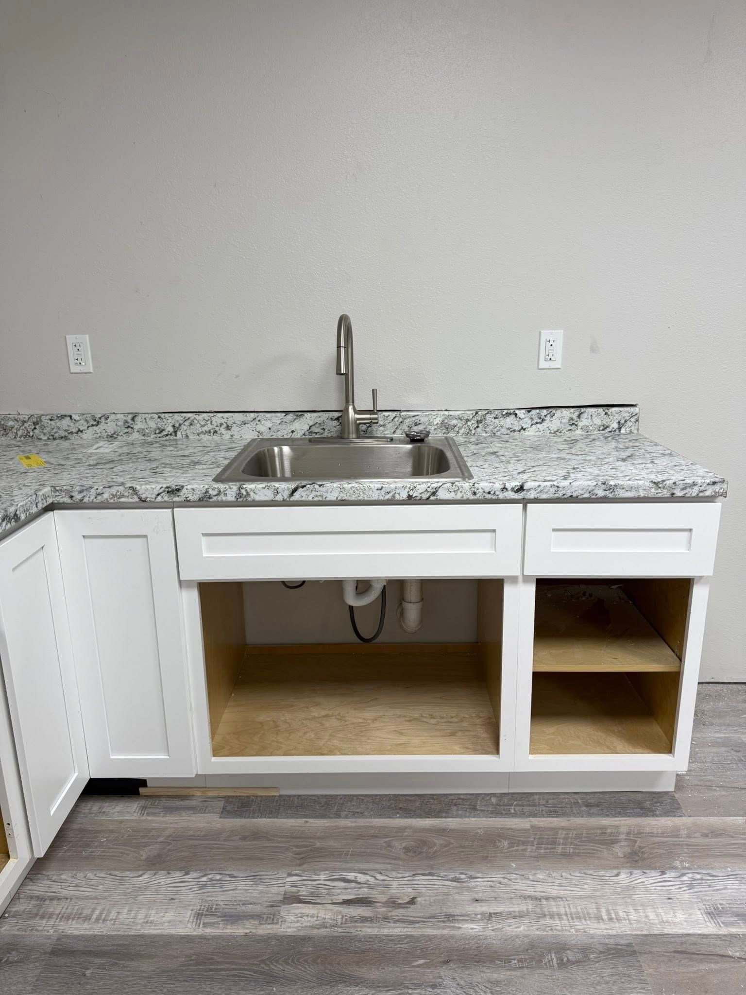 White cabinets with granite countertop and stainless steel sink. Open space below the sink.