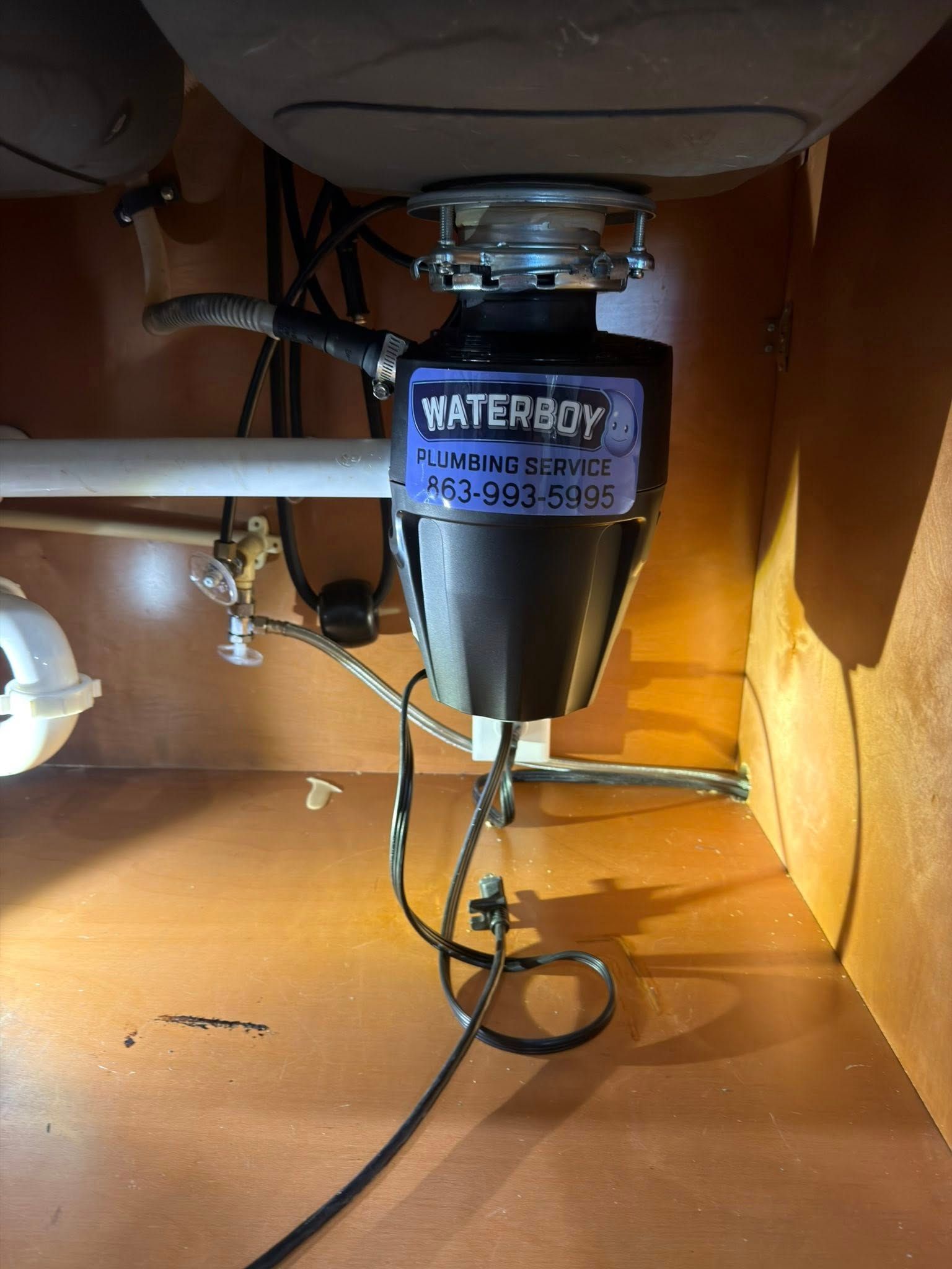 Garbage disposal under a kitchen sink. Black disposal unit with a blue label in a brown cabinet.