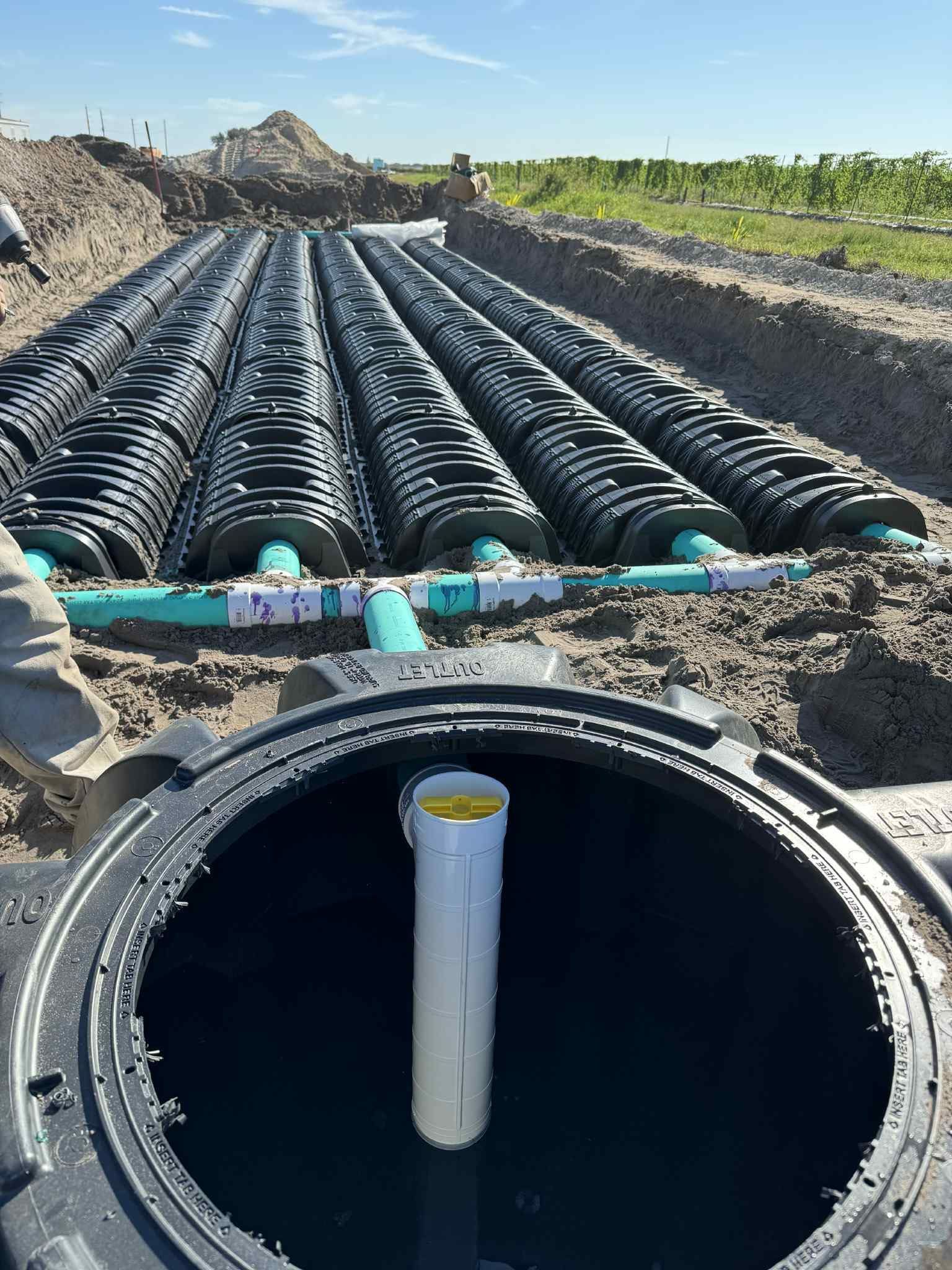 Septic system installation in progress: black plastic tanks, long black drainage tubes, and turquoise pipes in a dirt trench.