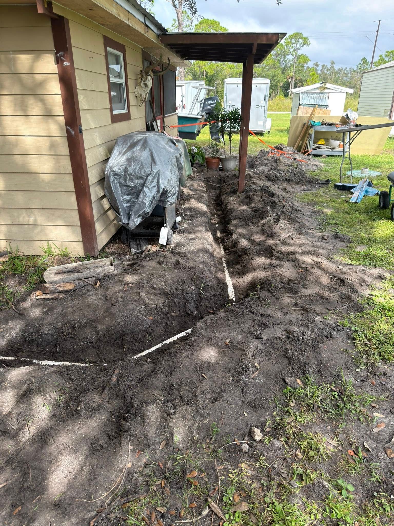 Trench dug alongside a beige house for plumbing; plastic pipes visible.