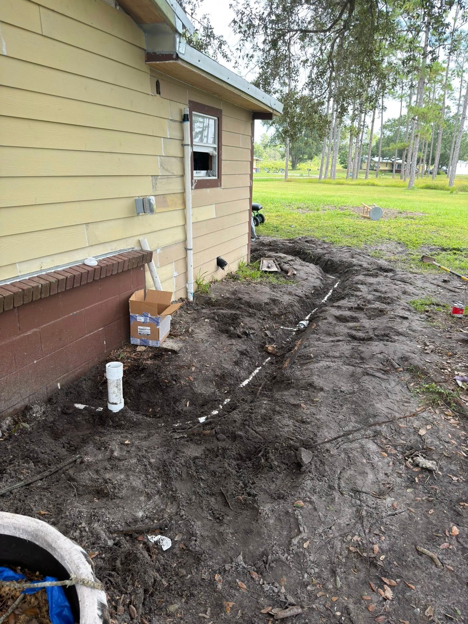 Construction site with trench and white PVC pipes near a beige house and green grass.