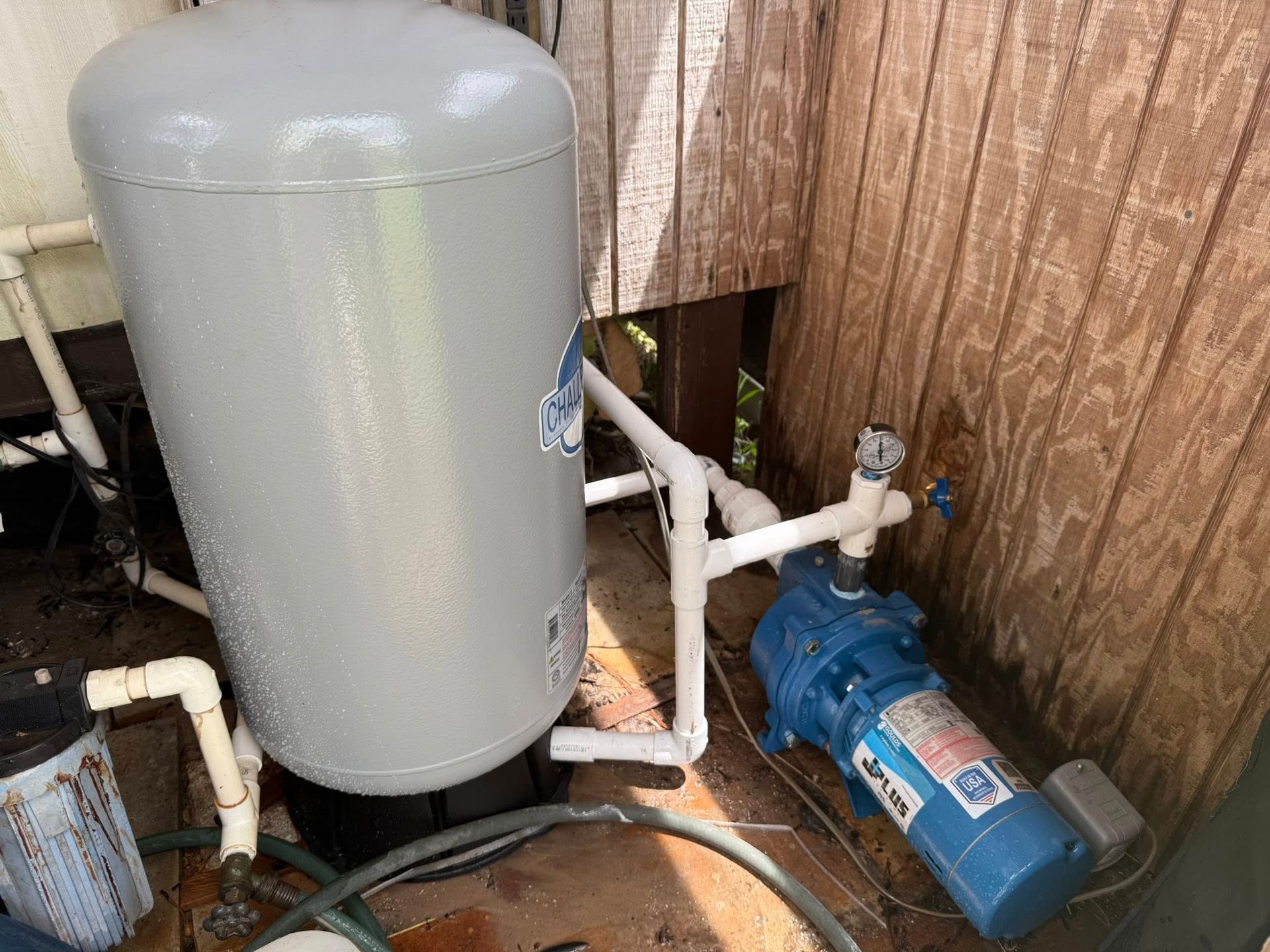 Water well pump system outdoors; includes a blue pump and a gray tank.