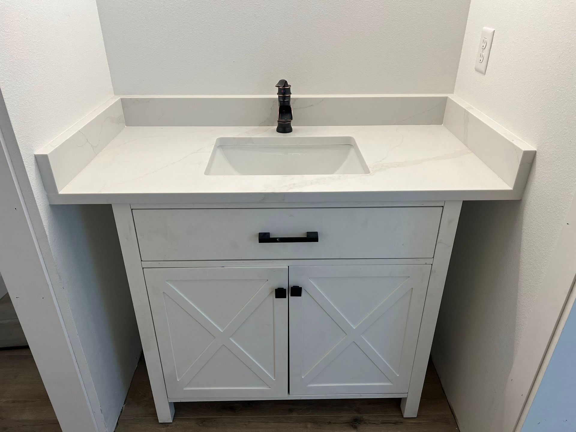 White bathroom vanity with a white countertop and black faucet.
