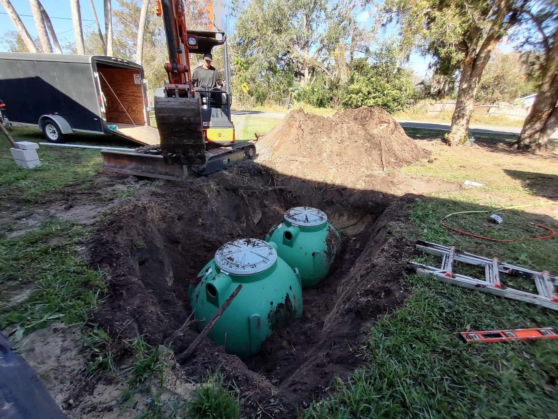 Two green septic tanks in an excavated hole. An excavator sits above.
