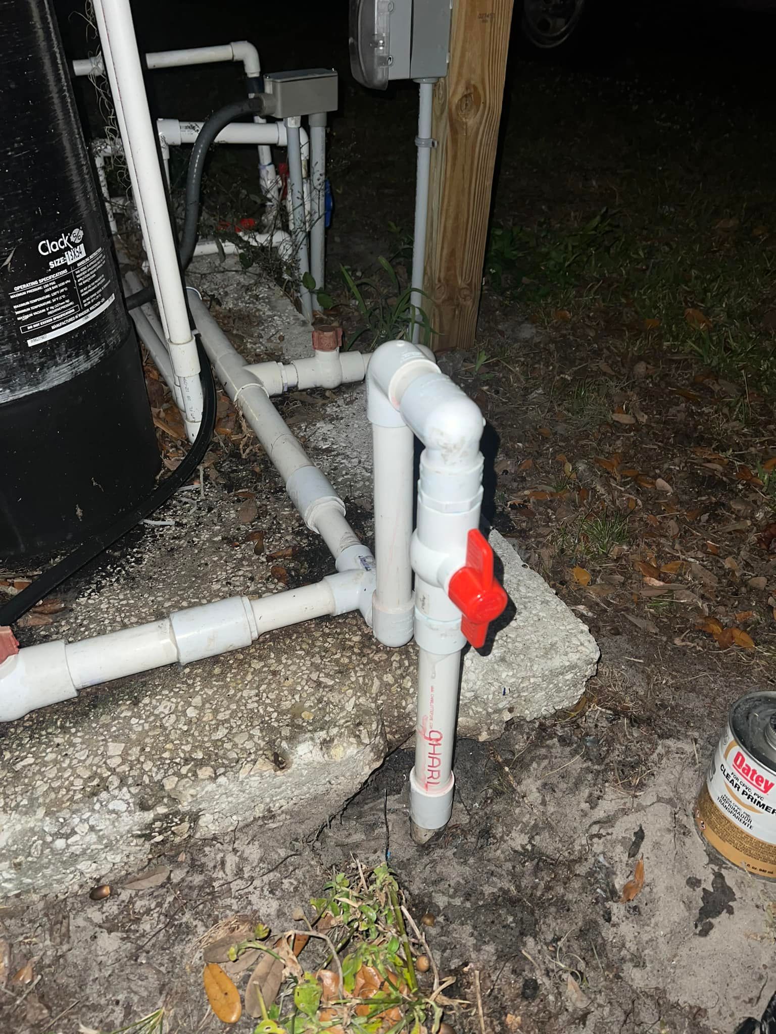 PVC pipes with a red-handled valve near a pool system's concrete base.