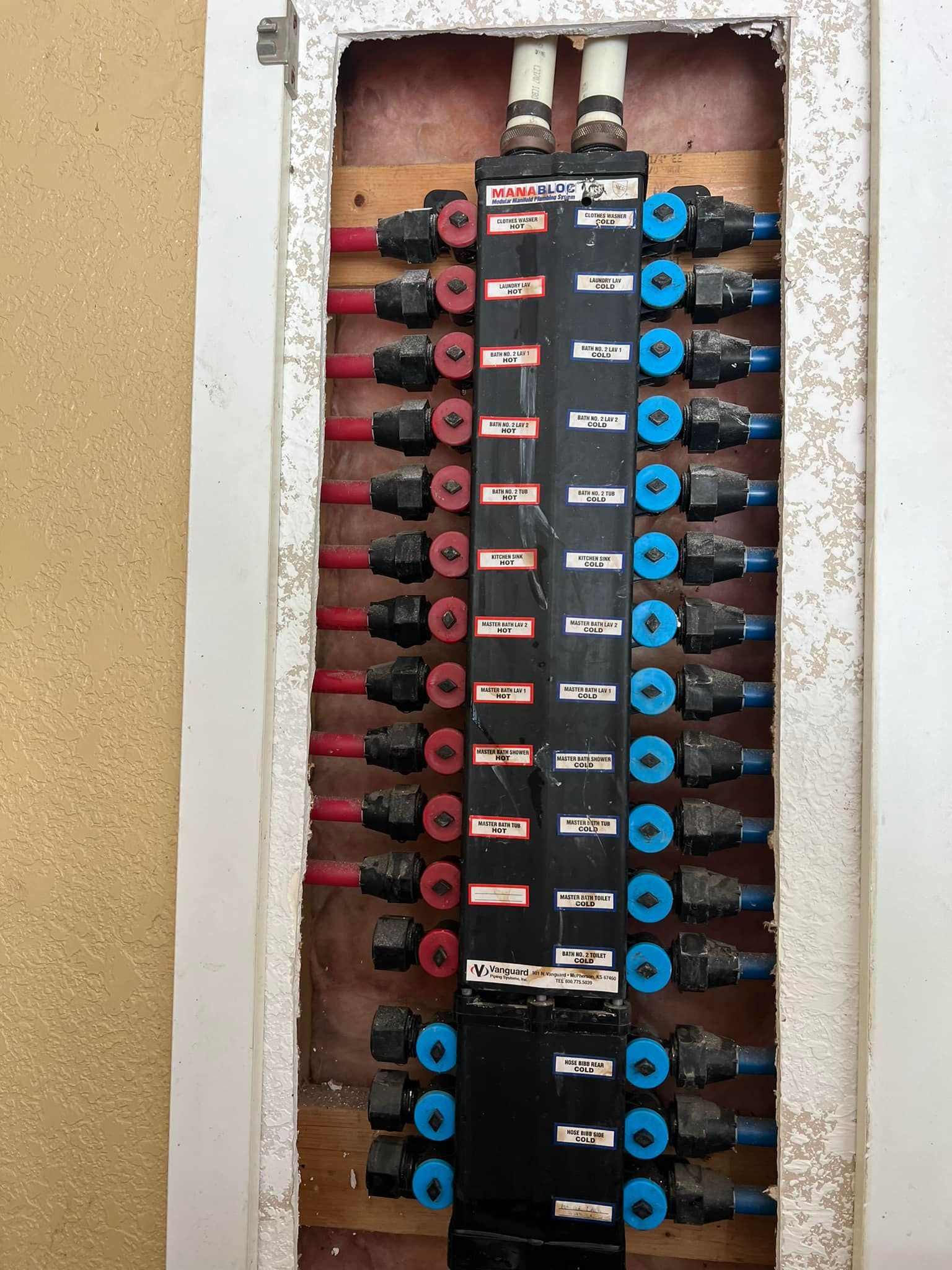 Black manifold with red and blue pipes, inside a wall.