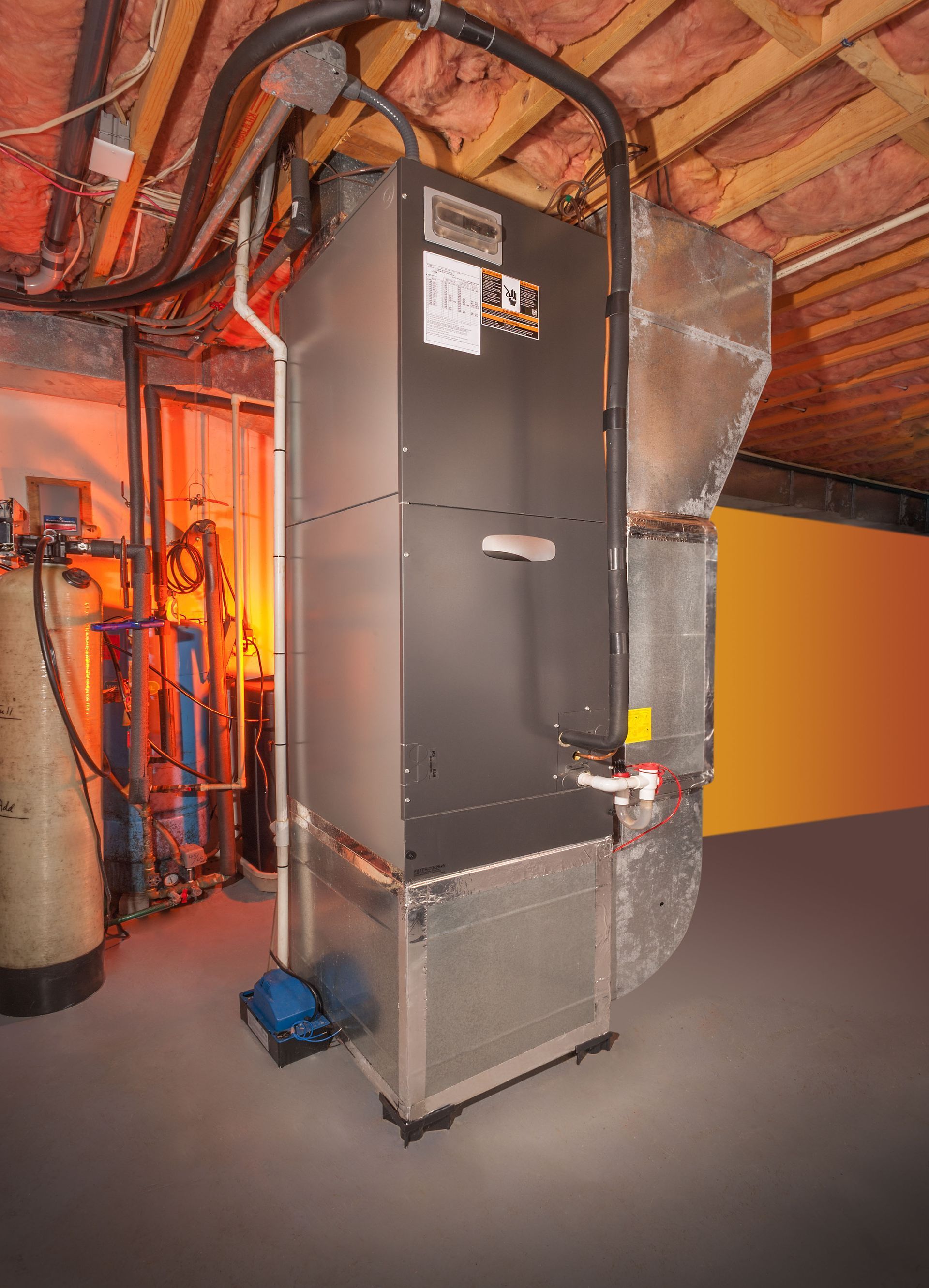 Large gray HVAC furnace in an attic with exposed rafters and ductwork