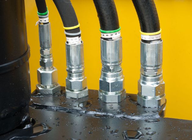 Hydraulic hoses and metal fittings connected to a black machine base against a yellow background