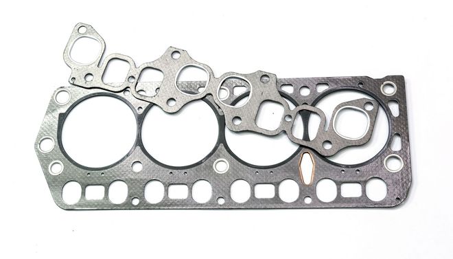 Silvery engine cylinder head gasket with round openings on a white background