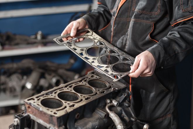 Mechanic holding a cylinder head gasket over an engine block in a garage