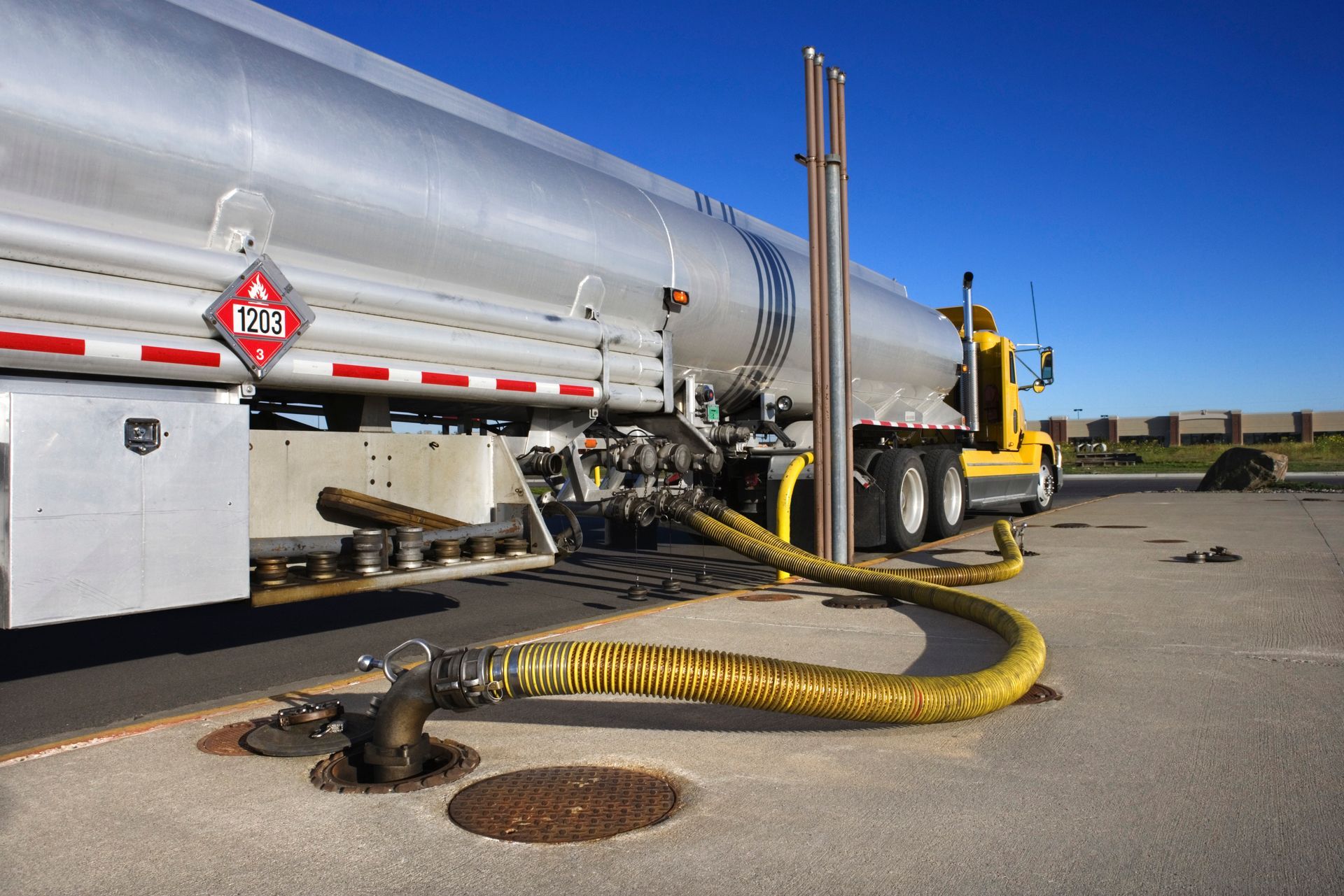 Silver fuel tanker truck with yellow hoses on a paved lot under a clear blue sky