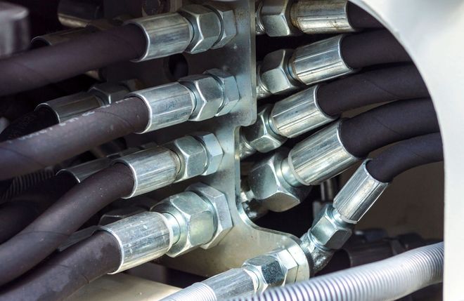 Close-up of coiled black and silver industrial hoses and metal hydraulic fittings inside a compartment