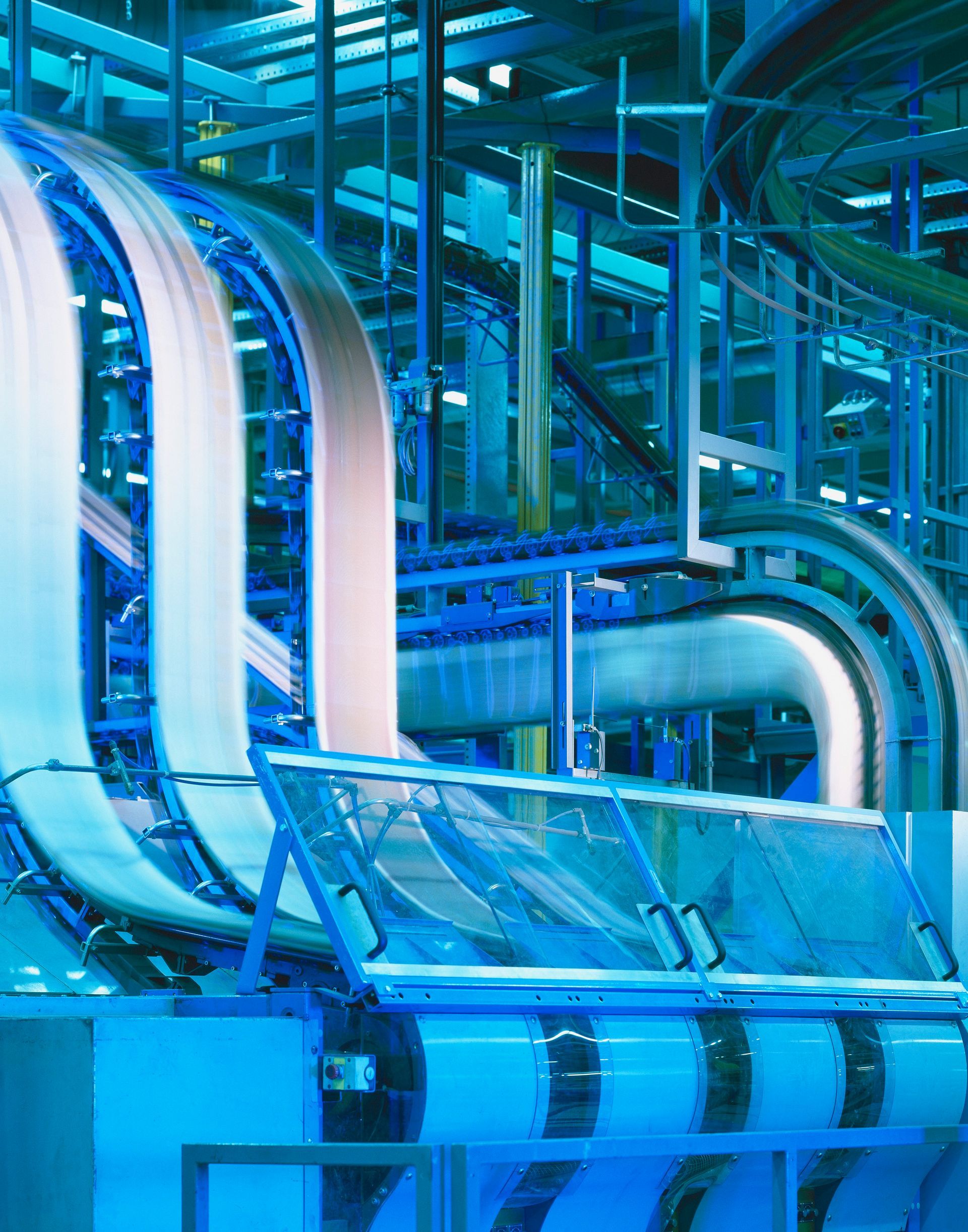 Blue-lit industrial conveyor system inside a factory with curved metal tracks and pipes.