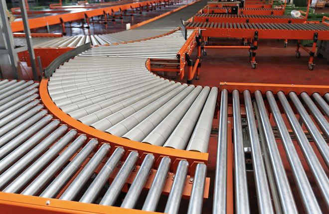 Orange roller conveyor with white and silver rollers in an industrial warehouse