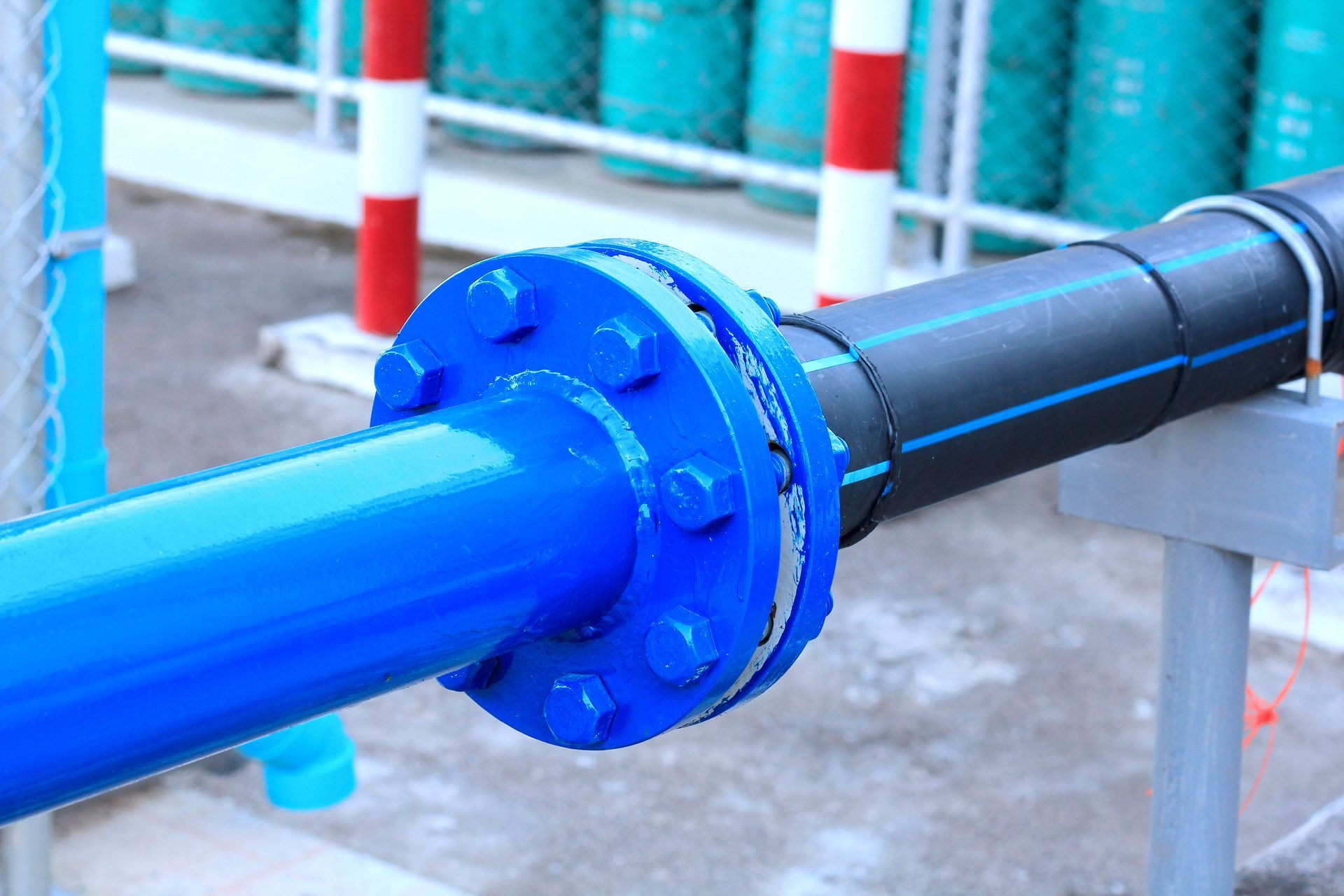 Blue and black industrial pipes connected by a flanged joint on a metal support frame