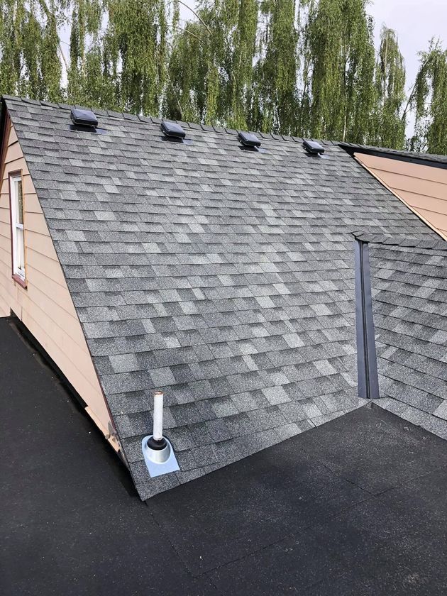 Roof with gray shingles, several missing patches, and a nearby white vent under cloudy sky.