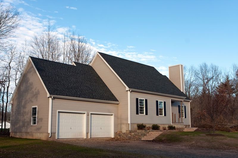 Suburban beige house with attached two-car garage and leafless trees under a blue sky