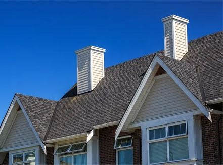 Two white chimneys on a gray shingled house roof against a clear blue sky