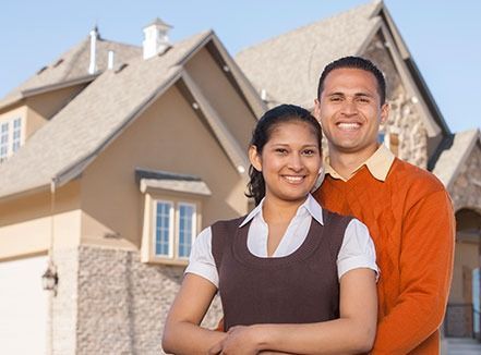 Two smiling homeowners standing in front of a new house with stone accents