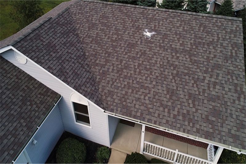 Aerial view of a gray-shingled house roof with a small white mark near the center