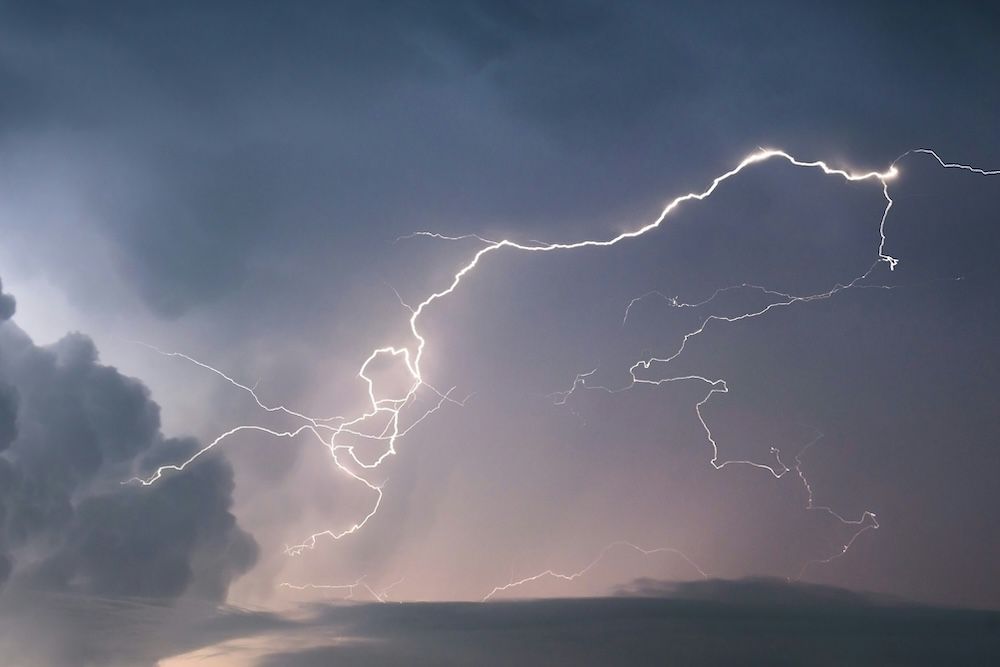 Lightning streaks across a dark cloudy sky over a distant landscape.