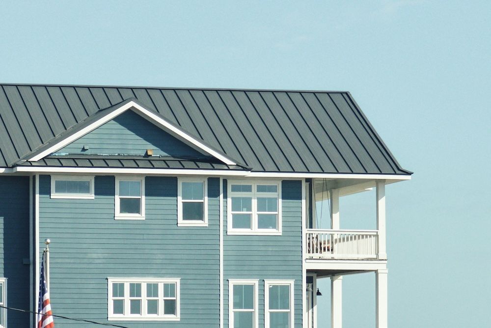 Blue seaside house with white trim and metal roof, showing balcony and windows