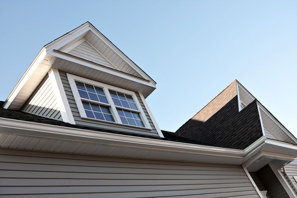 Low-angle view of a house roof and dormer windows against a blue sky