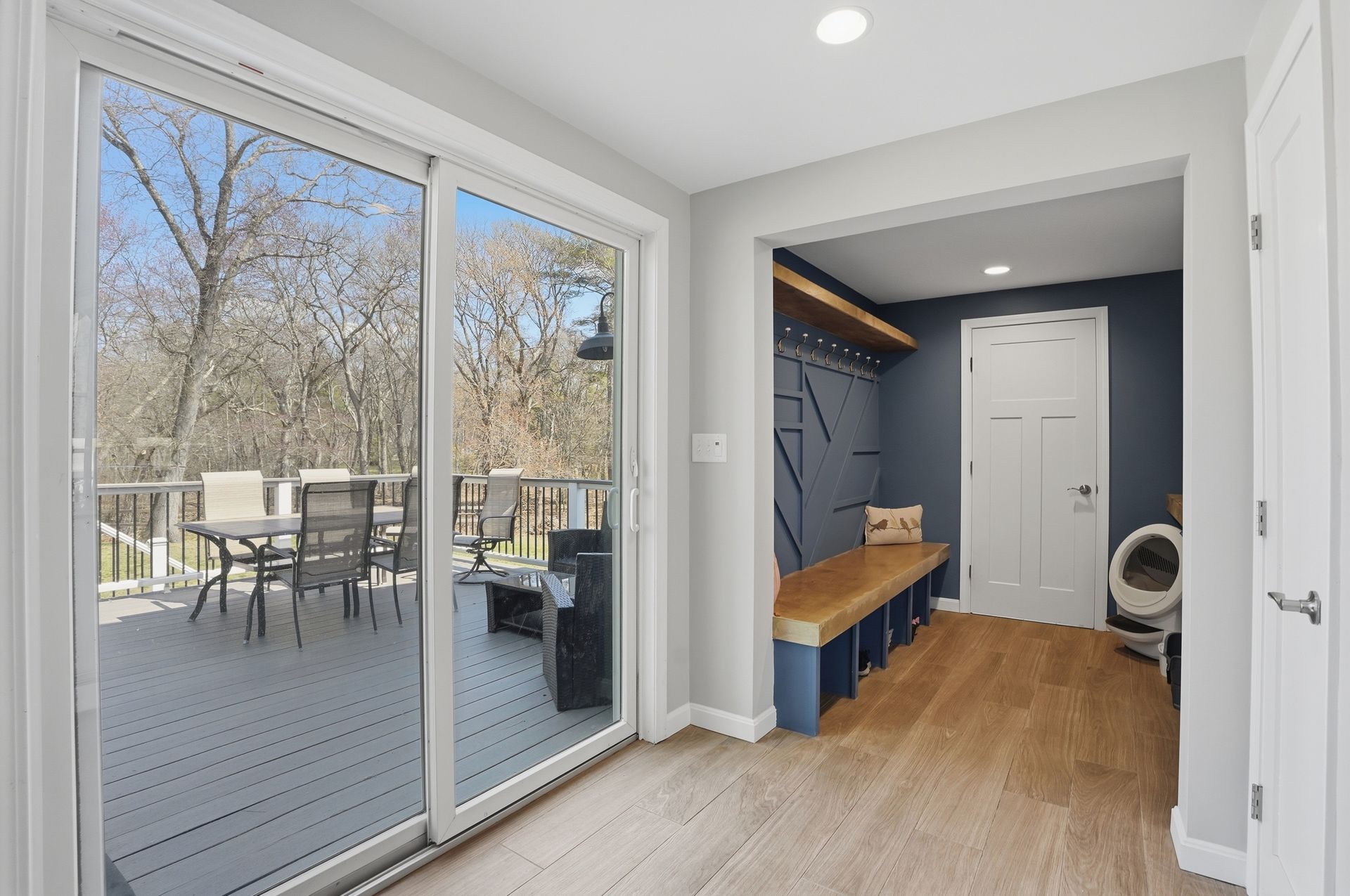 Bright mudroom with sliding glass doors, wood floor, bench, hooks, and a small bathroom area.