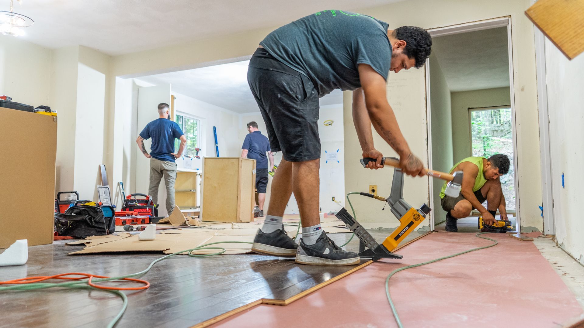 Workers using tools during a home renovation with exposed flooring and construction materials.