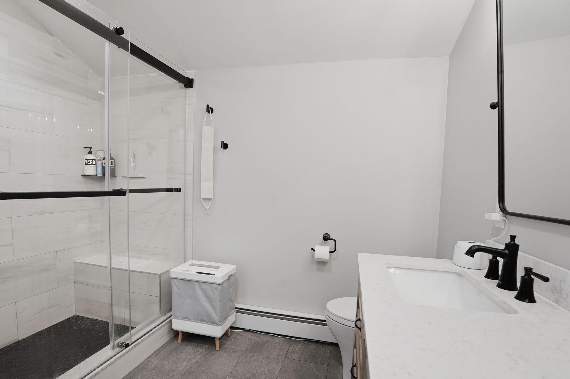 Modern white bathroom with black hardware, shower, toilet, and vanity mirror