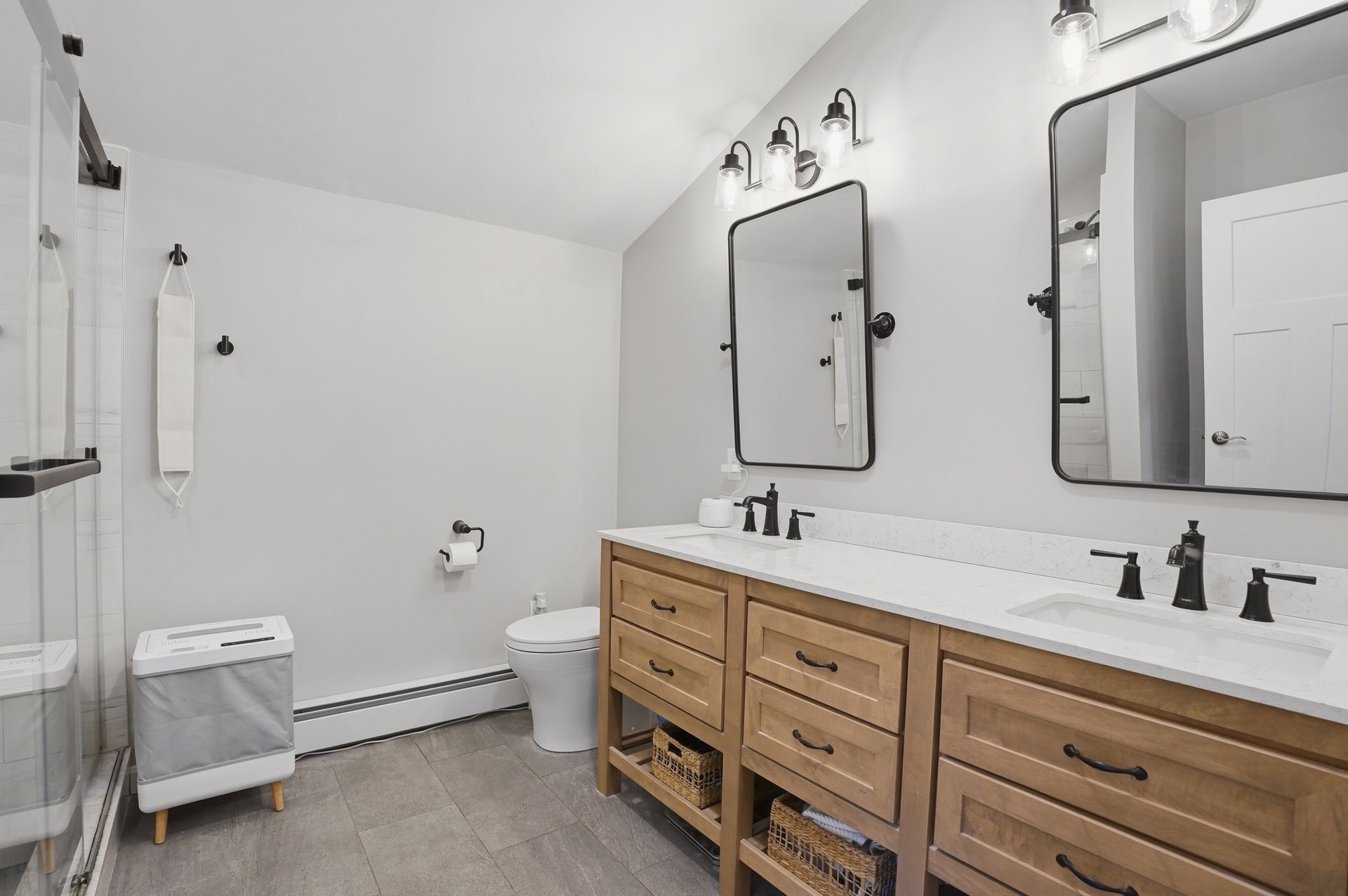 Bright white bathroom with wood vanity, black fixtures, mirrors, toilet, and shower curtain