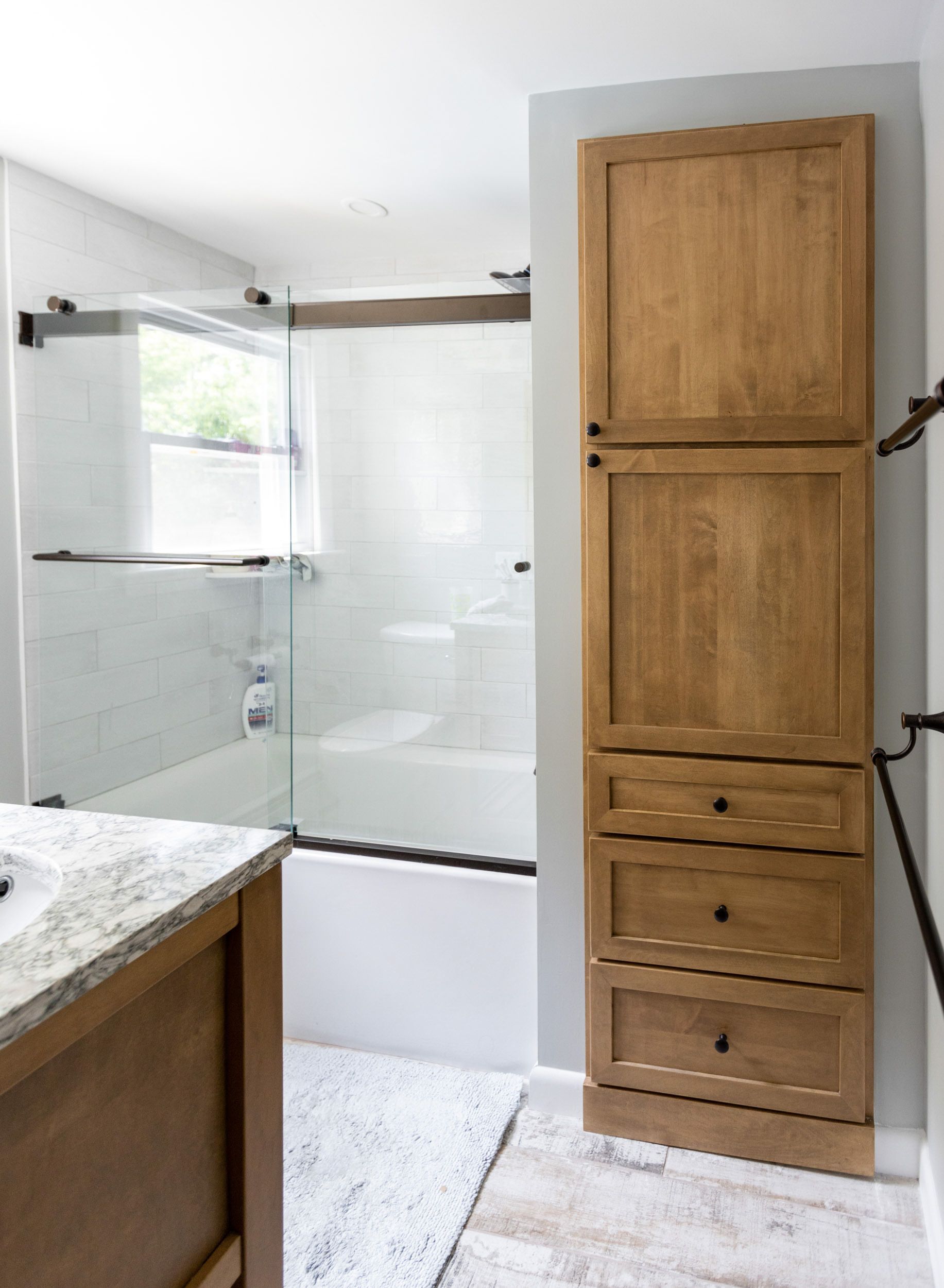 A bathroom featuring a wooden storage cabinet, a vanity with a stone countertop, and a shower with a sliding glass door.