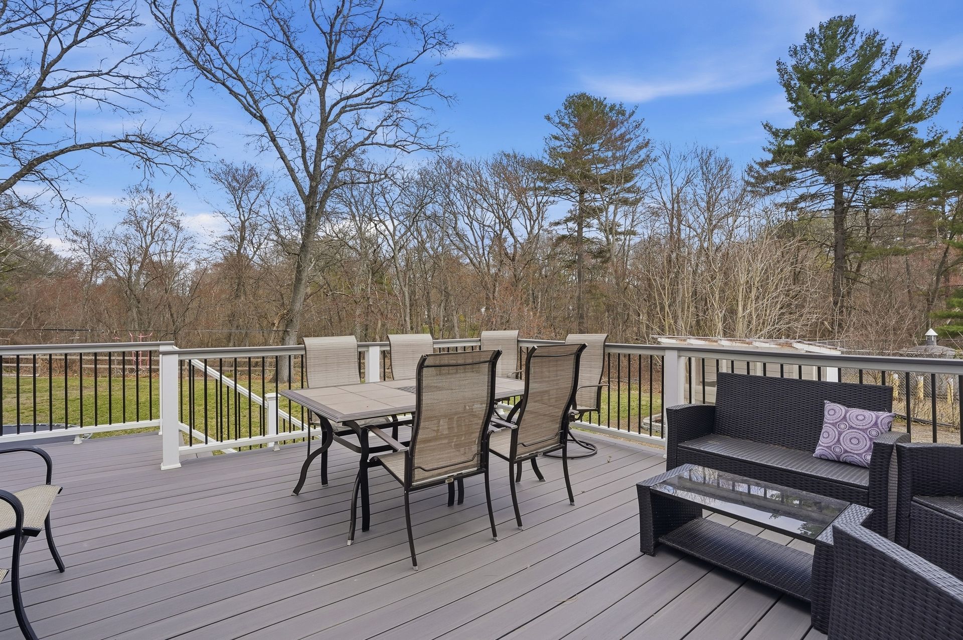 Deck with patio furniture overlooking a wooded yard under a clear blue sky