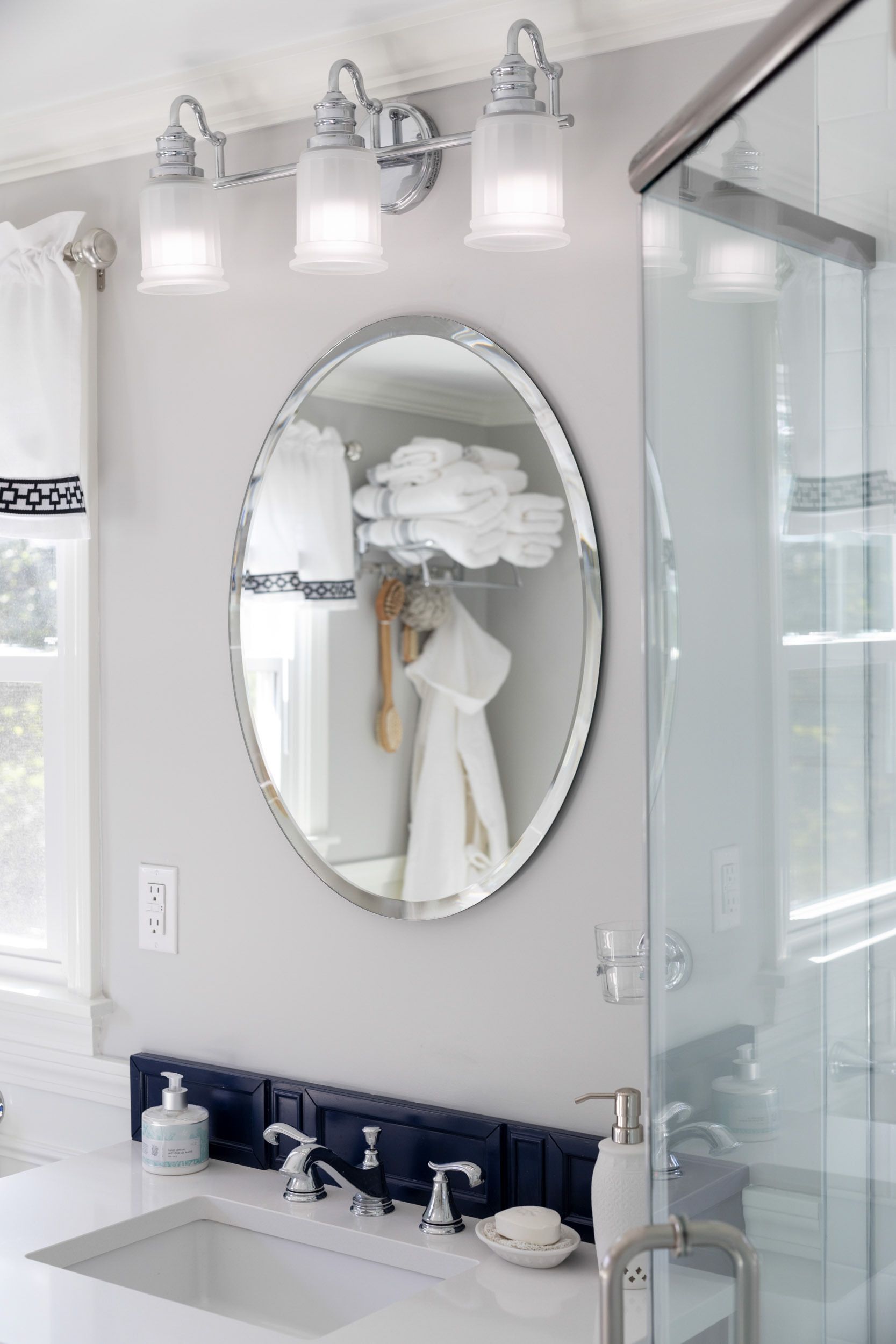A modern bathroom vanity with a white countertop, dark blue tiled backsplash, oval mirror, and three glass pendant lights.
