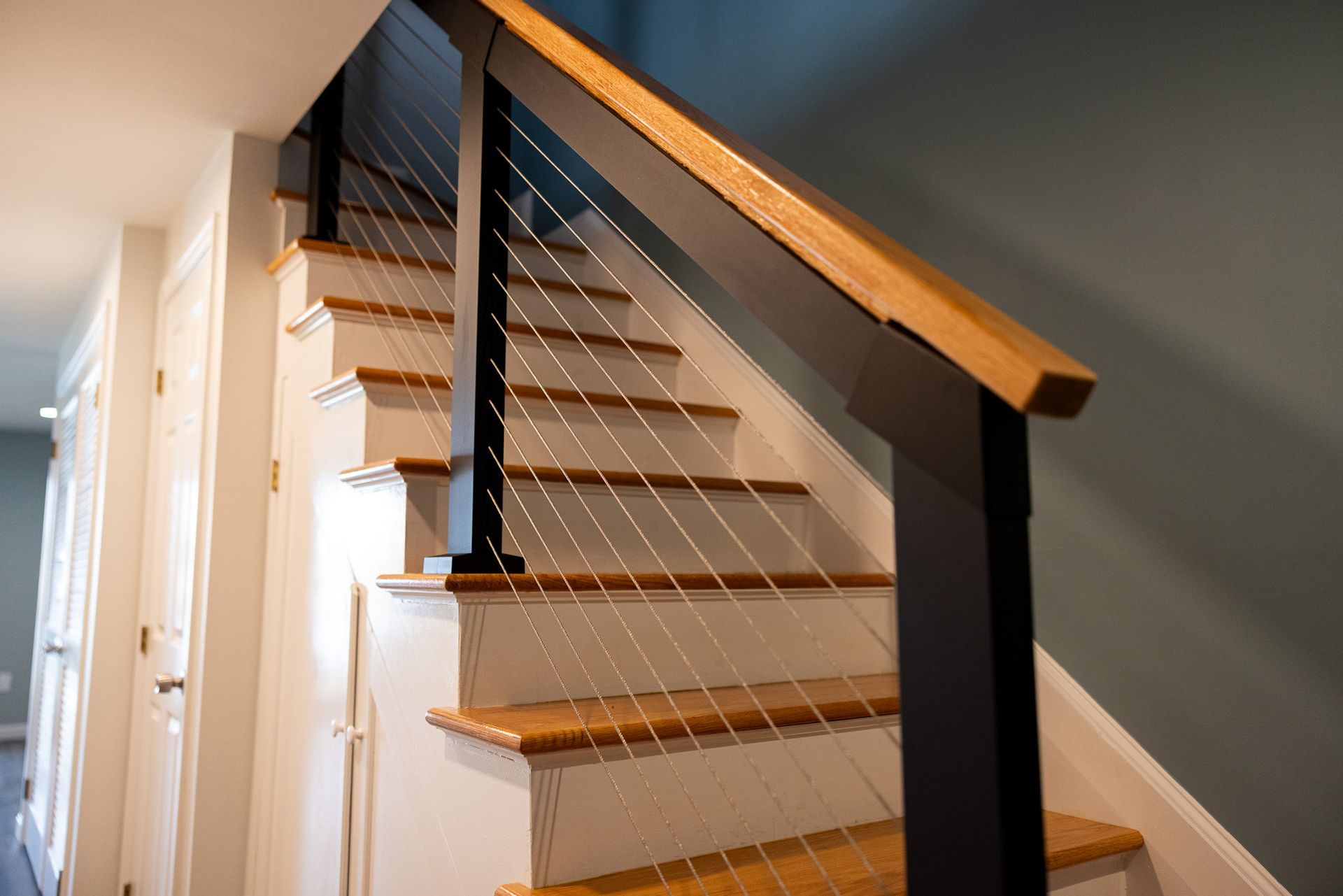 A modern staircase featuring wooden treads, black posts, and a cable railing system against a dark blue wall.