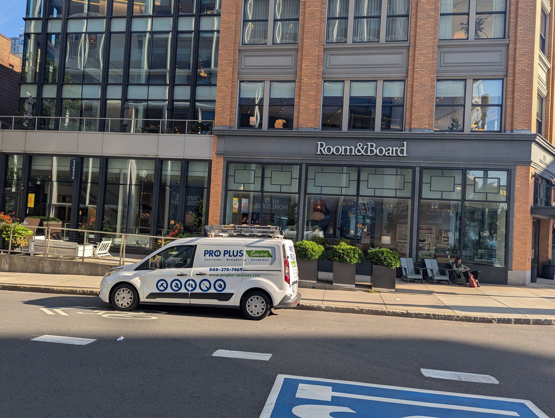 A white van parked on a street in front of a modern glass-fronted building and a brick storefront labeled Postmark.