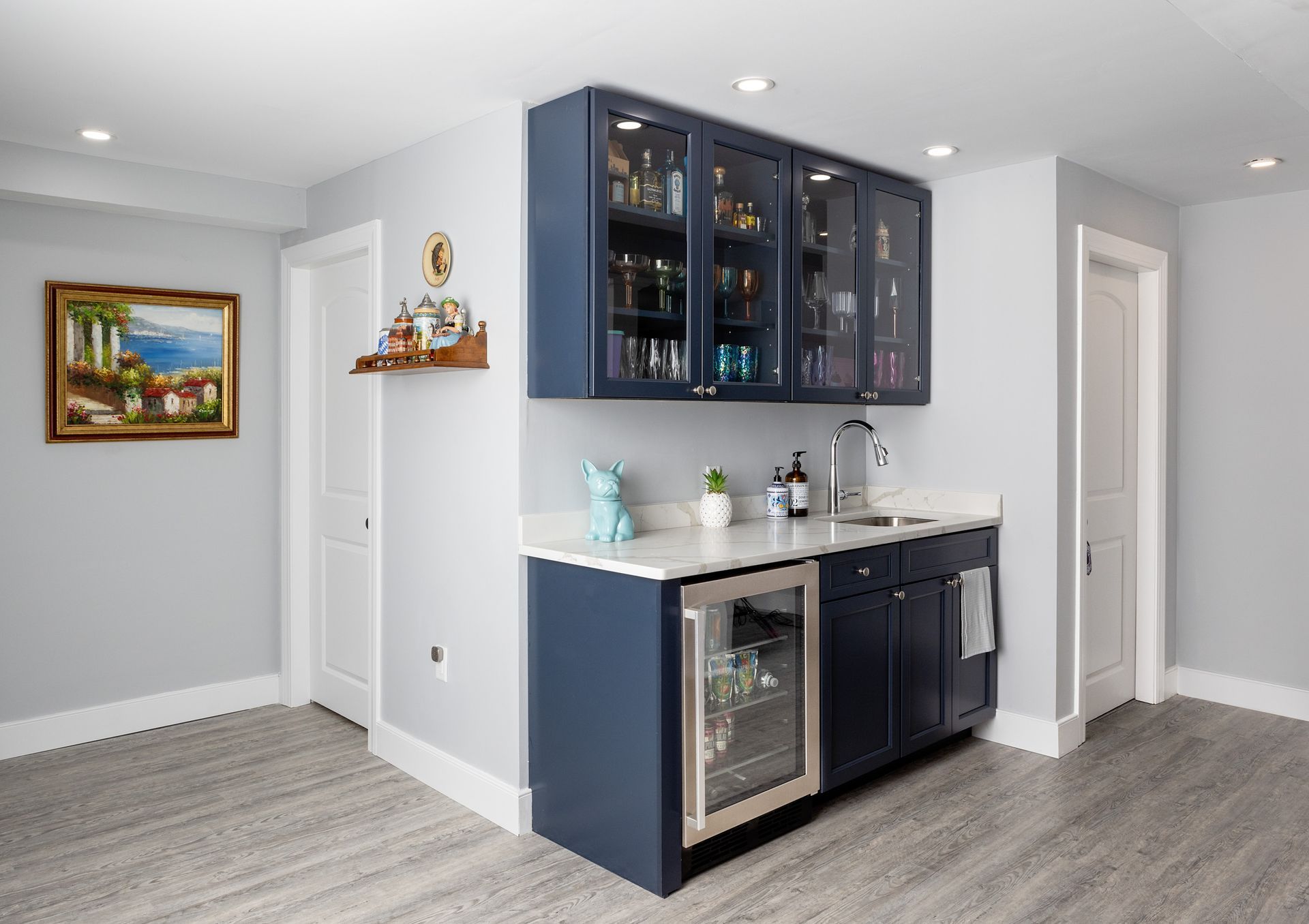 A small home wet bar featuring navy blue cabinets, a built-in wine fridge, and glass-front upper cabinets.