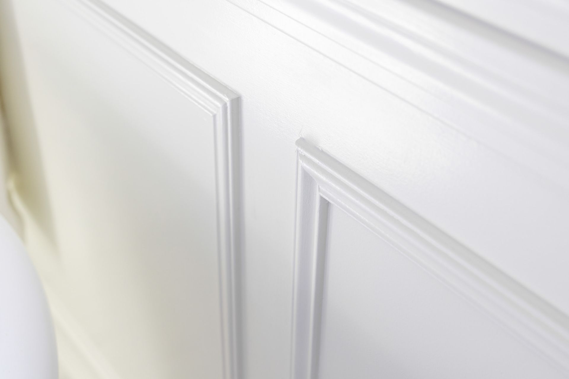 A close-up of white wooden wainscoting featuring decorative molding panels on a wall.