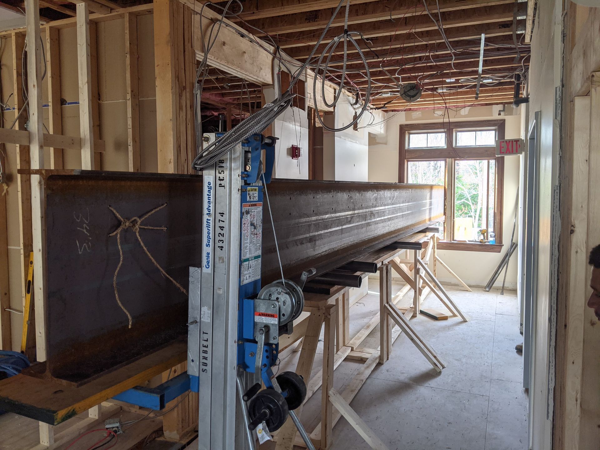 A heavy steel beam is positioned on a temporary lift and wooden supports within a room undergoing structural renovation.