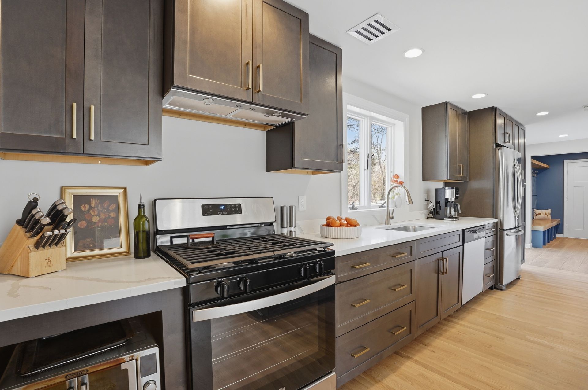 Modern kitchen with dark cabinets, stainless stove, white countertops, and hardwood floor