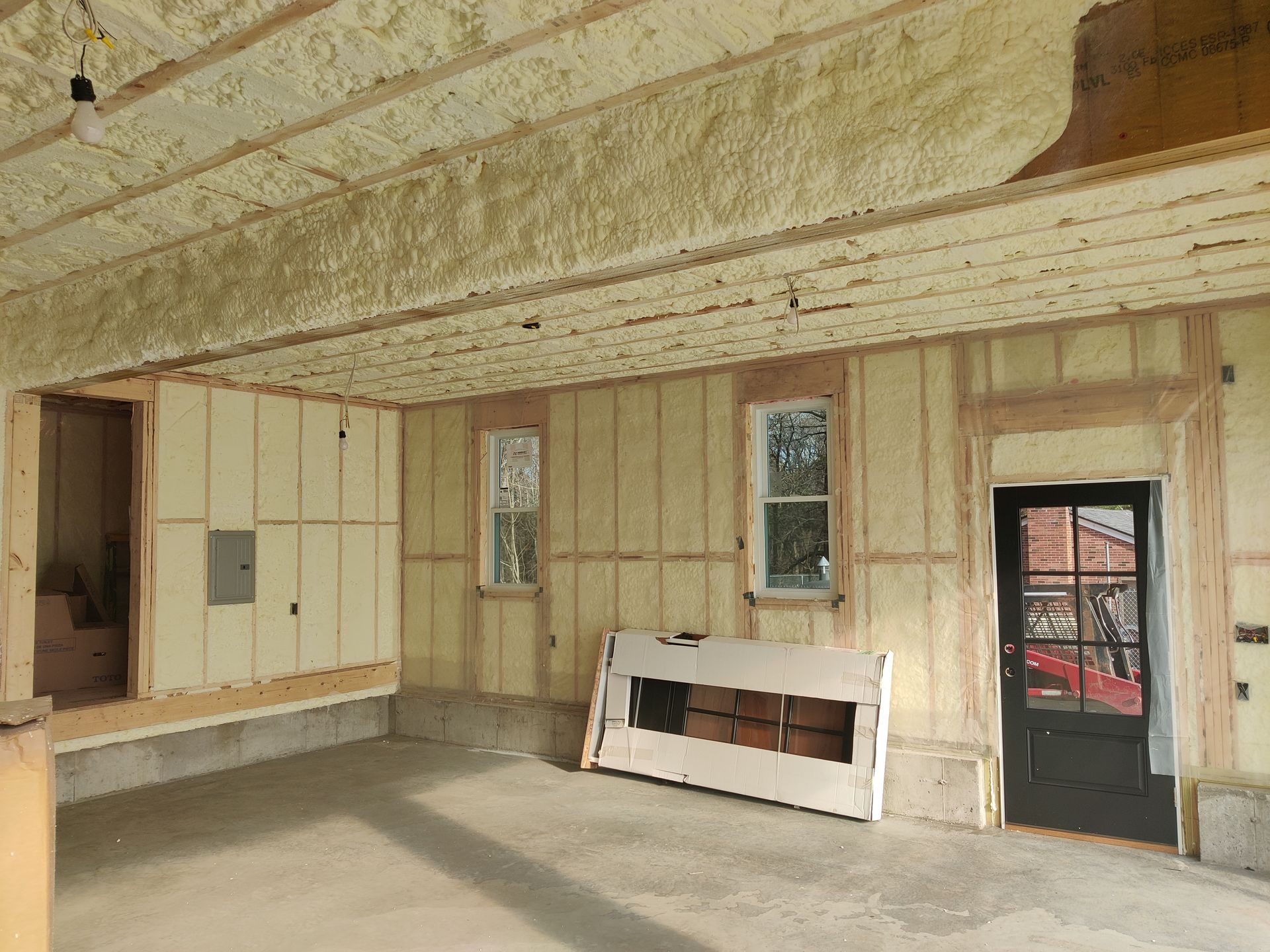 An interior room under construction with insulated walls and ceiling, two windows, and a dark glass door.